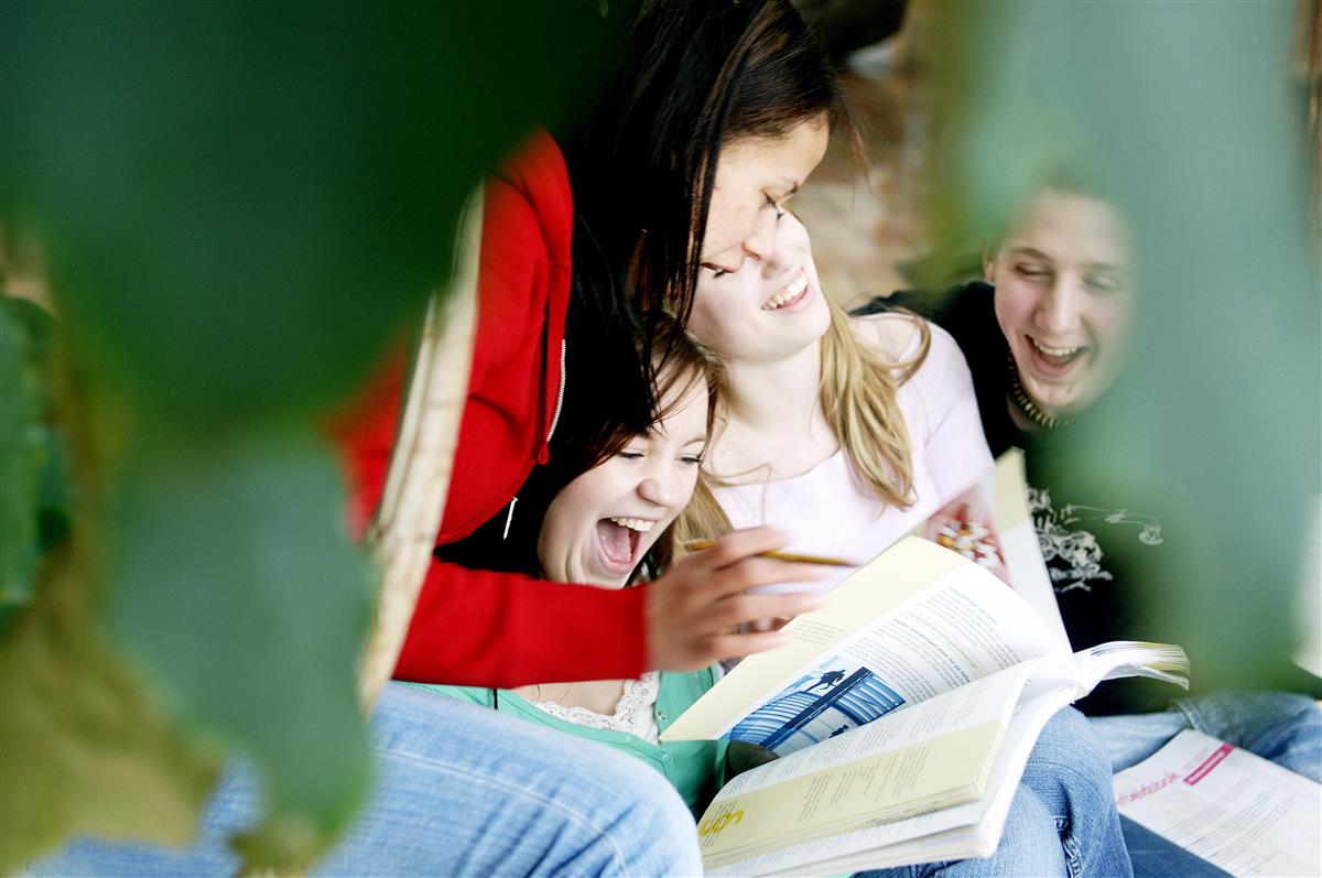 Glade ungdommer som sitter tett sammen og leser bok - Klikk for stort bilde