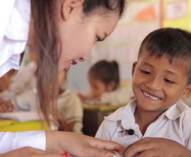 Lærer som hjelper liten gutt på skole i Kambodsja - Klikk for stort bilde